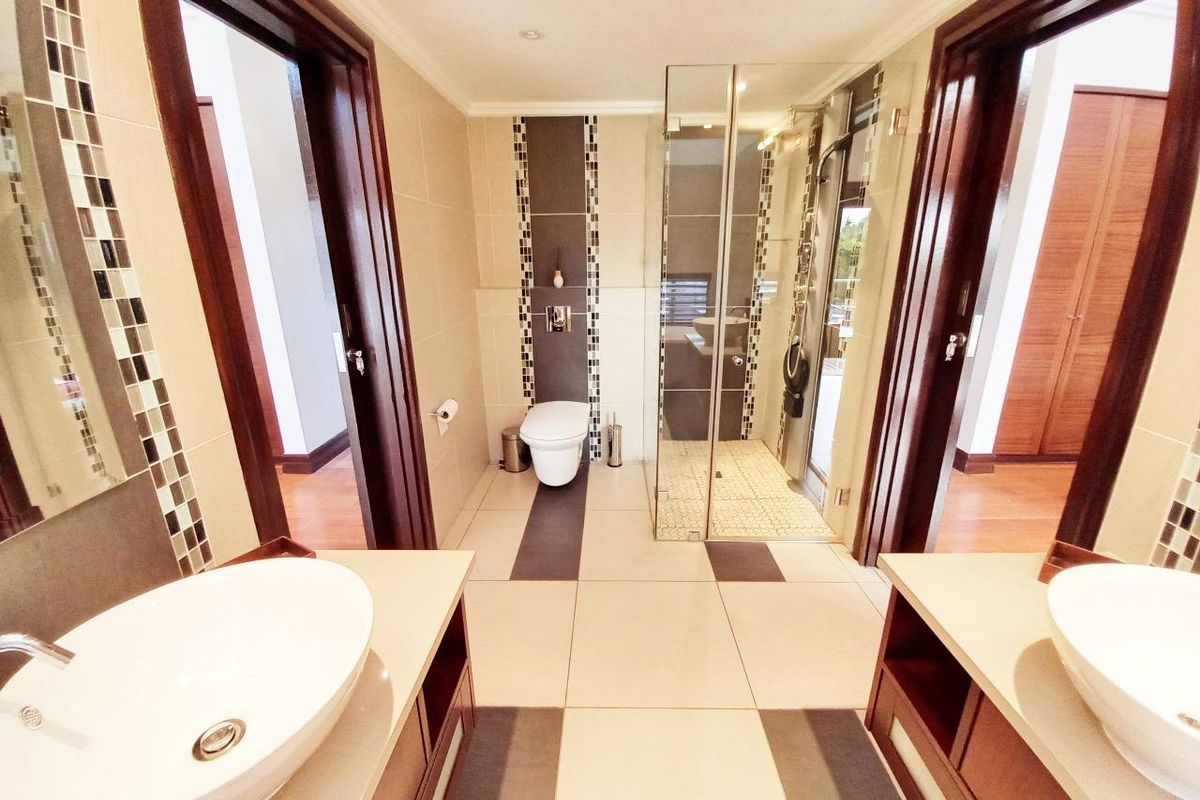 Modern bathroom featuring a double vanity with vessel sinks, a walk-in glass shower, and a wall-mounted toilet with decorative mosaic tile accents.