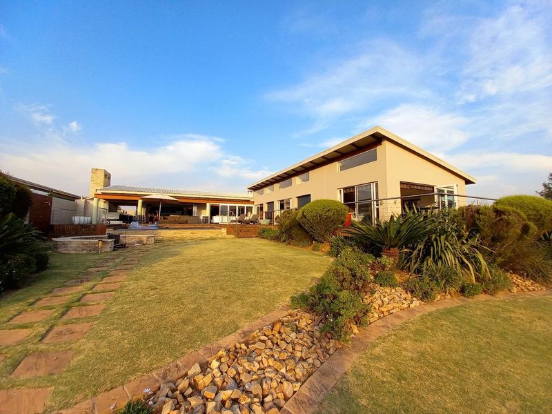 Spacious rear exterior view featuring a landscaped garden, stone pathways, a covered patio area, and a modern house structure with large sliding glass doors.