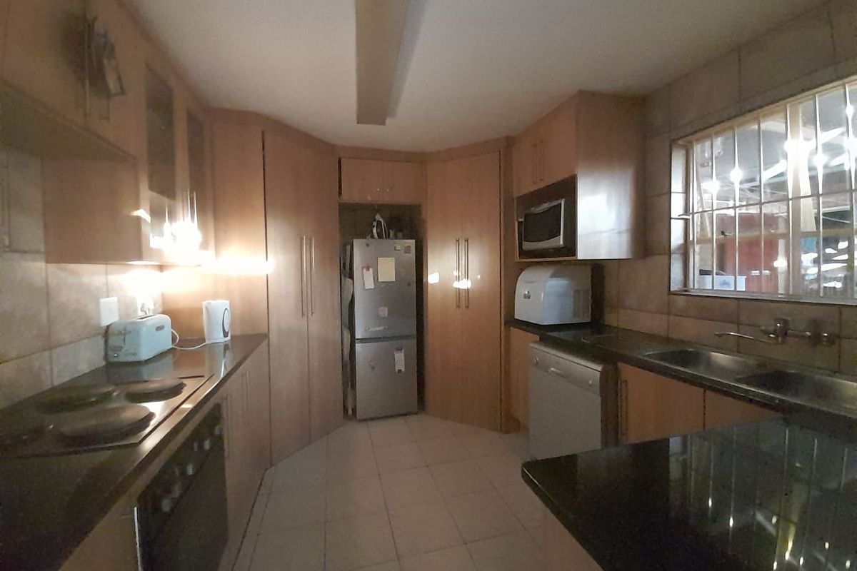 A functional kitchen featuring wooden cabinetry, granite countertops, an electric hob, built-in oven, and tiled finishes throughout.