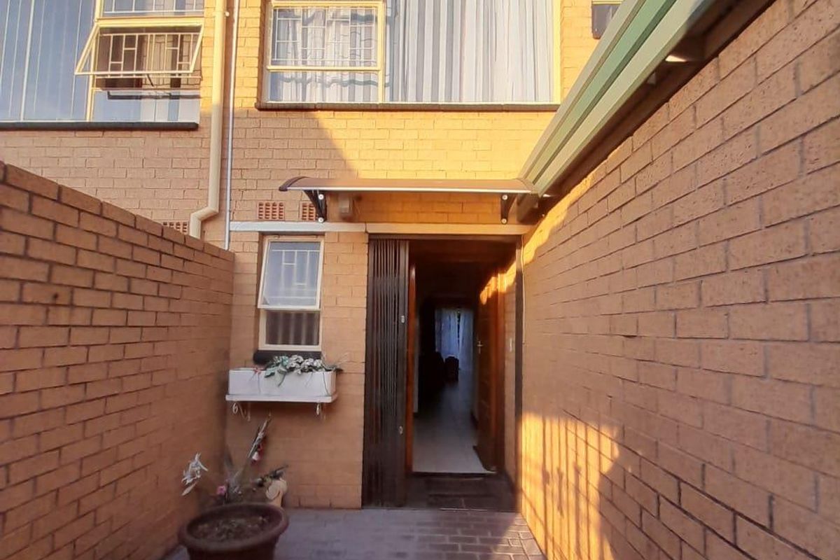Rear exterior view of a townhouse featuring brick paving, enclosed brick boundary walls, and a covered entrance leading into the home.