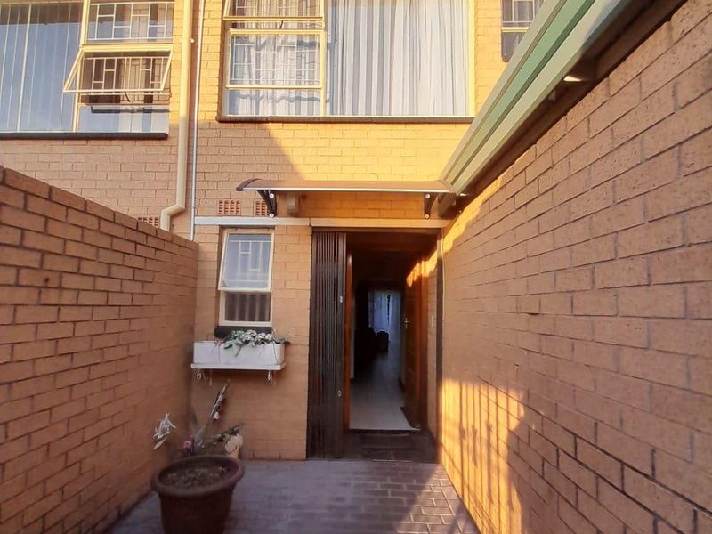 Rear exterior view of a townhouse featuring brick paving, enclosed brick boundary walls, and a covered entrance leading into the home.