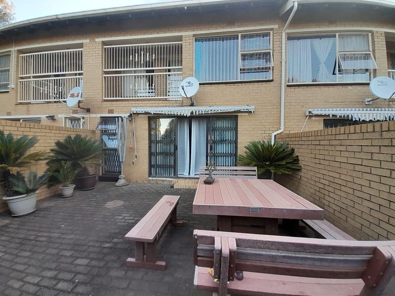 Rear exterior view of a townhouse featuring a paved patio area, brick facade, and secure sliding door access.
