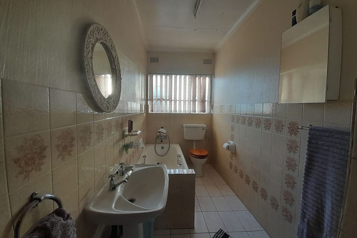 A dated bathroom featuring a pedestal basin, built-in bathtub, and toilet, finished with traditional wall tiling and floor tiles.