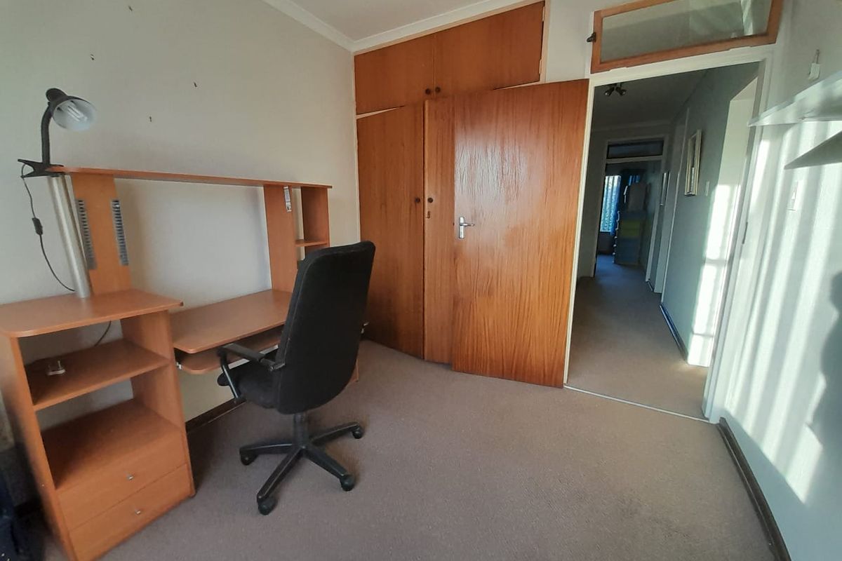 A bedroom featuring built-in wooden cupboards, carpeted flooring, and a transom window, leading into a hallway.