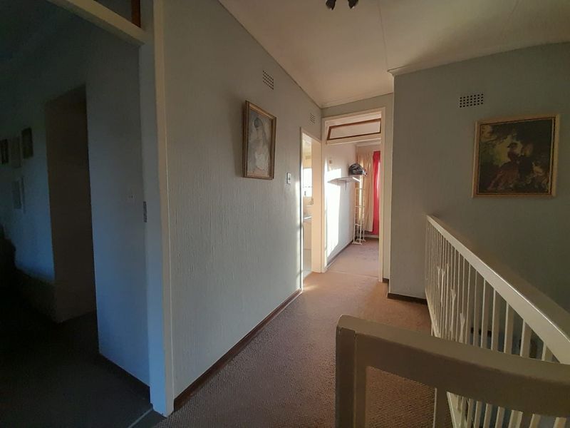 A functional upper-level hallway featuring a staircase railing, neutral wall finishes, and access to adjacent rooms.