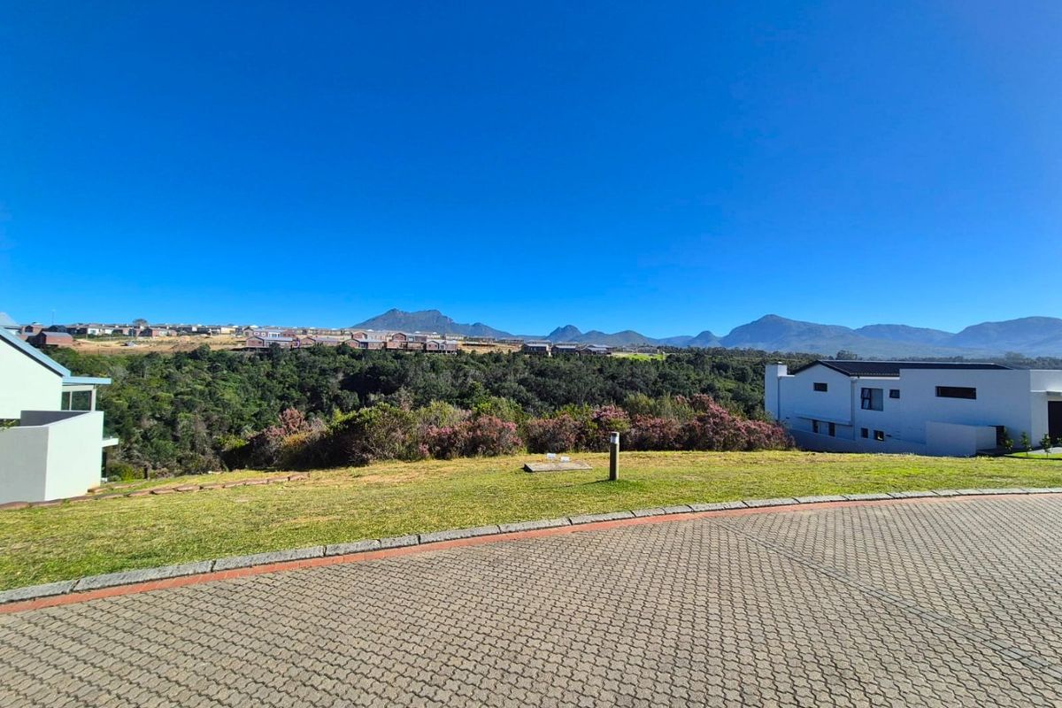A scenic view of the surrounding landscape and distant mountains from a residential vacant land plot with a paved driveway.