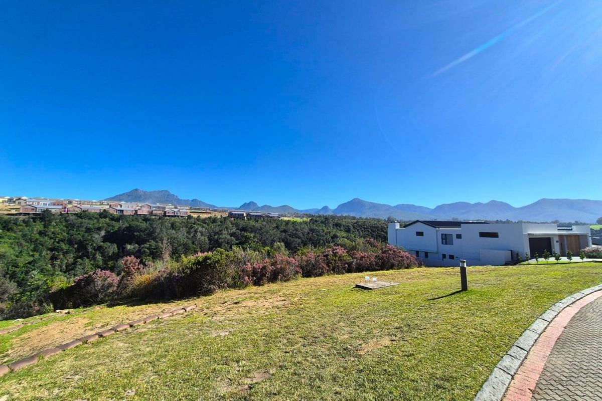A scenic view of the surrounding landscape and mountains from a residential vacant land plot with a paved driveway and manicured lawn.
