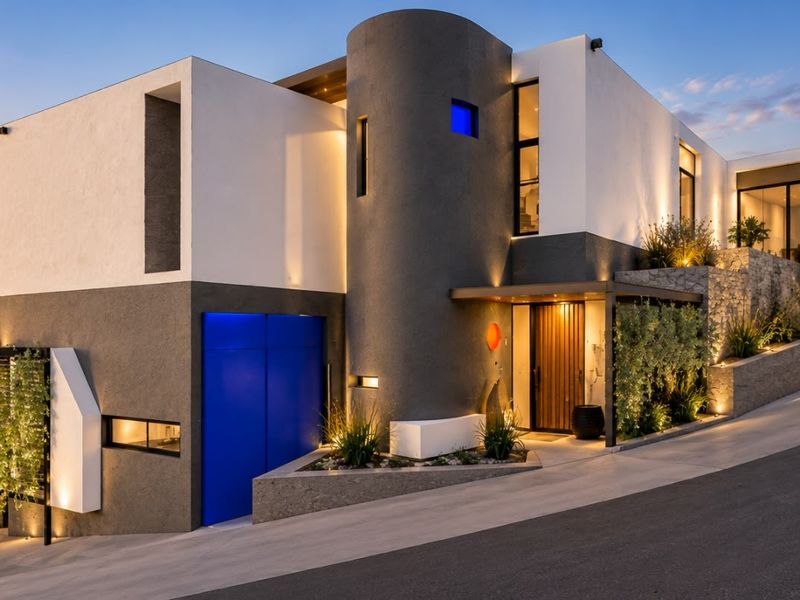 A striking modern architectural residence featuring a multi-level facade, integrated lighting, and a sleek concrete driveway set against a scenic landscape.