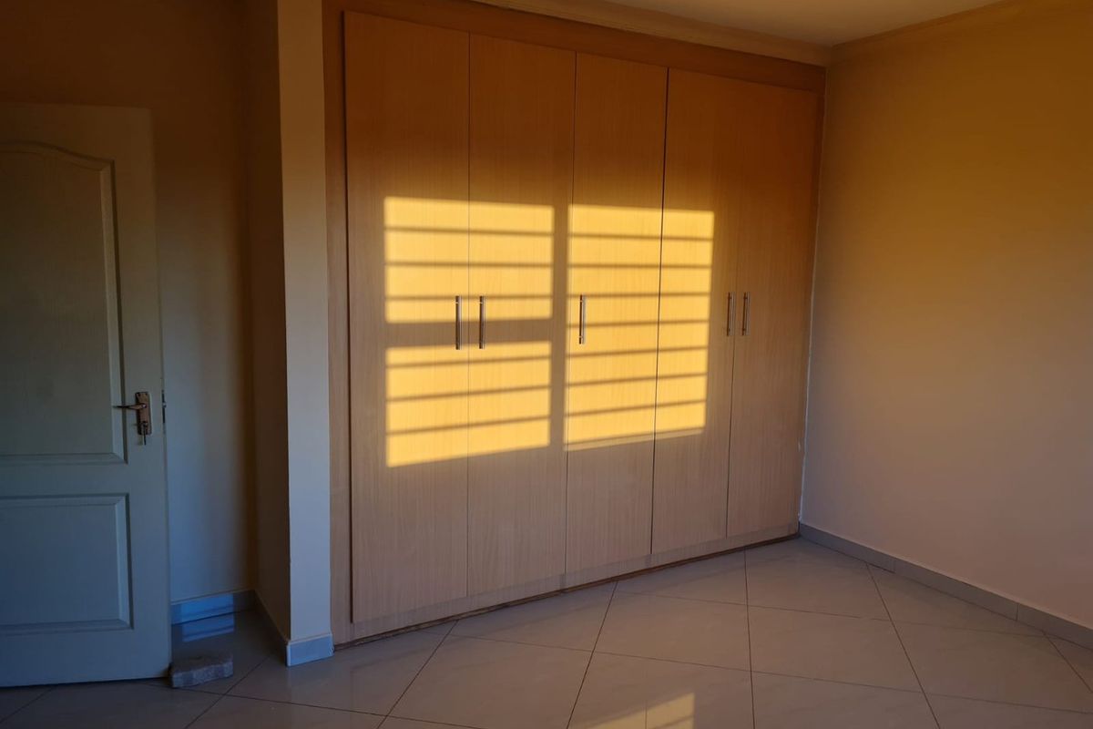 A bedroom featuring built-in wooden cupboards and tiled flooring, illuminated by natural light casting window shadows across the cabinetry.