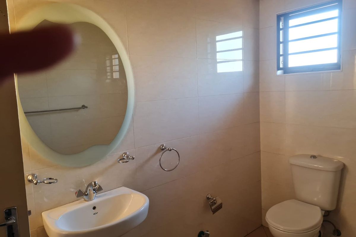 A clean, modern bathroom featuring a pedestal basin, wall-mounted mirror, and a standard toilet with tiled walls and a window for natural light.