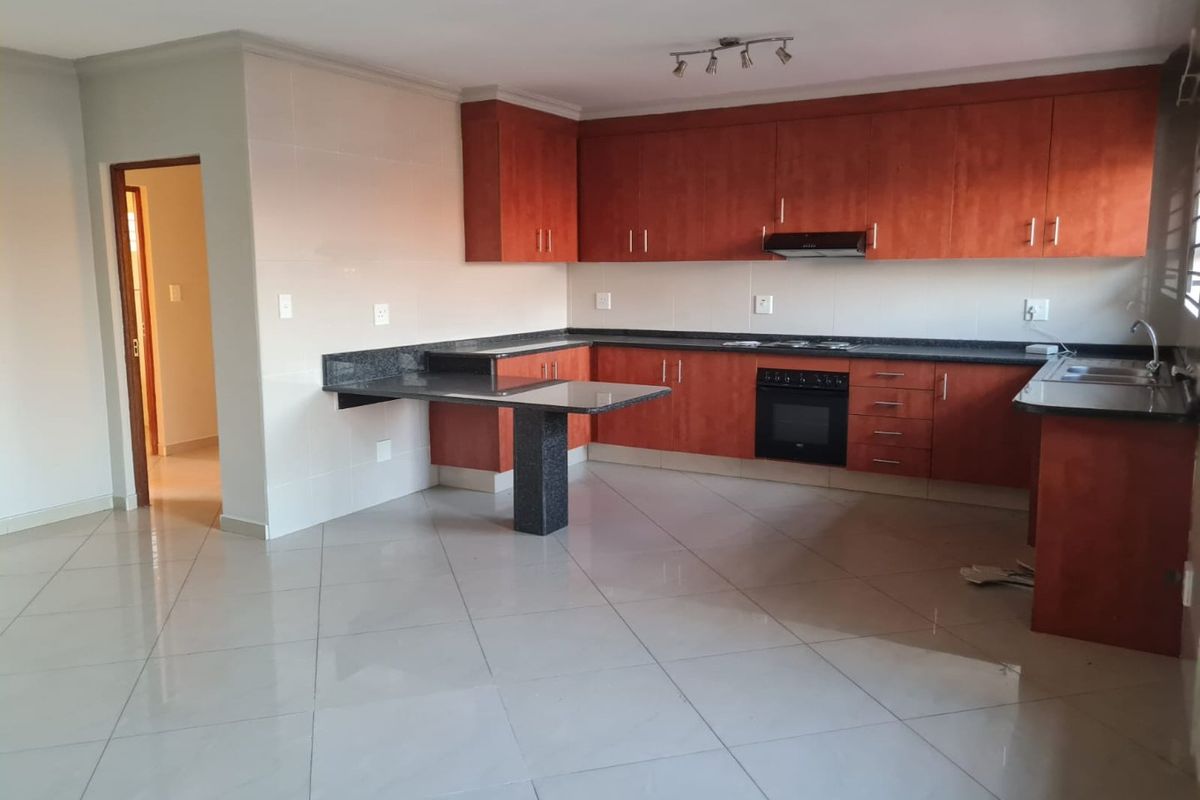 Open-plan kitchen featuring wooden cabinetry, granite countertops, built-in oven, hob, and extractor fan, set against tiled flooring.