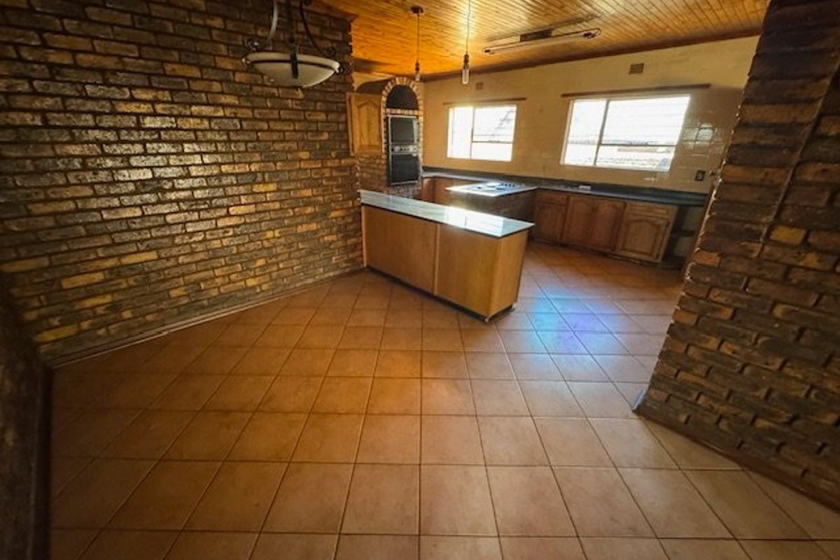 Spacious kitchen featuring exposed brick walls, wooden cabinetry, built-in oven, and tiled flooring, offering a rustic aesthetic with potential for modern updates.