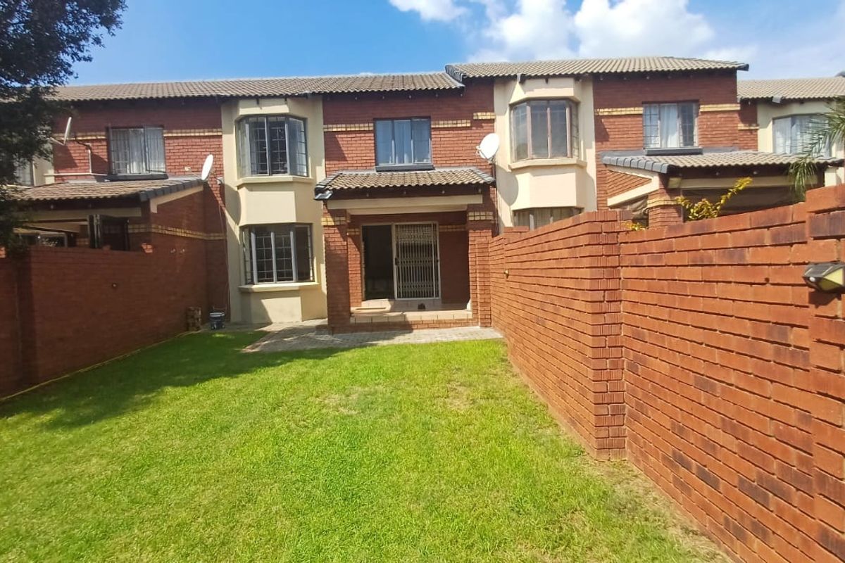 Rear view of a multi-story townhouse featuring a private garden, brick boundary walls, and a covered patio area with security gate access.