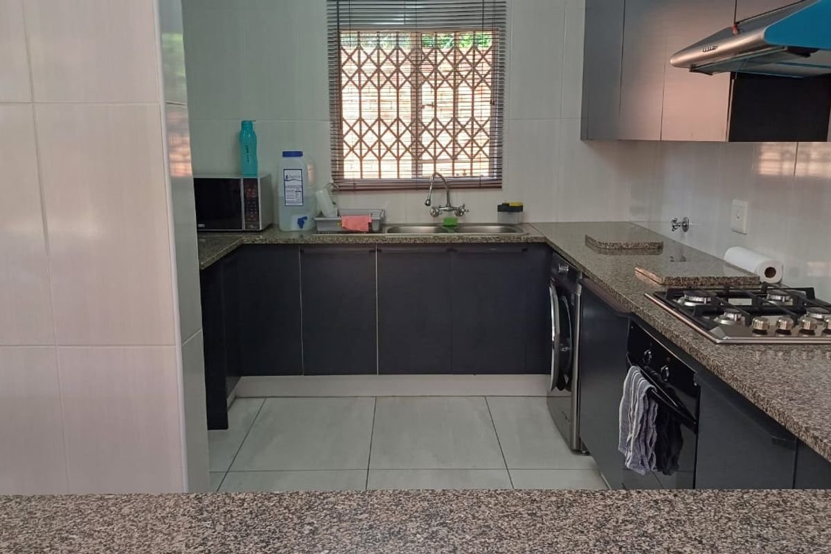 Functional kitchen featuring granite countertops, dark cabinetry, built-in gas hob, extractor fan, and integrated laundry appliance space.