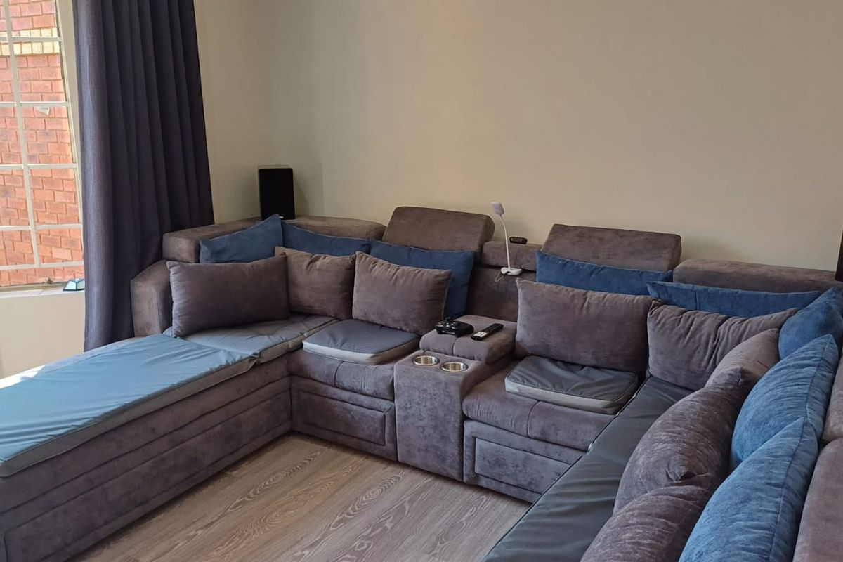 A comfortable living room featuring wood-look flooring, a large sectional sofa, and a window with curtains overlooking the exterior brickwork.