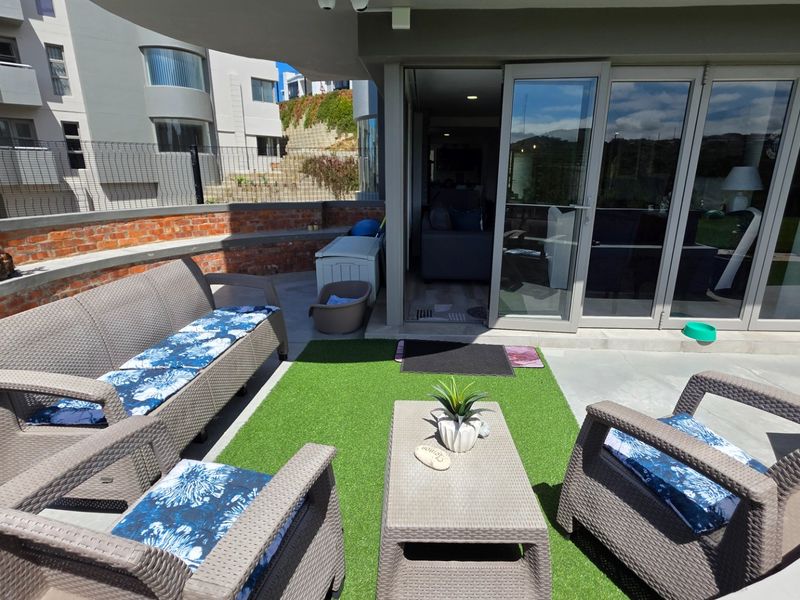 A spacious outdoor patio featuring concrete flooring, a built-in brick bench, and large sliding glass doors providing seamless access to the interior living area.