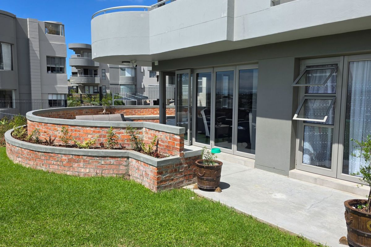Rear exterior view of the apartment featuring a concrete patio, brick retaining wall, and modern aluminium sliding doors leading to the interior living space.