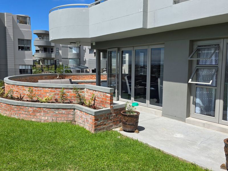 Rear exterior view of the apartment featuring a concrete patio, brick retaining wall, and modern aluminium sliding doors leading to the interior living space.