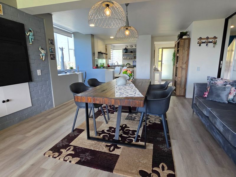 Open plan living and dining area featuring laminate flooring, an exposed brick feature wall, and a seamless transition to the kitchen space.