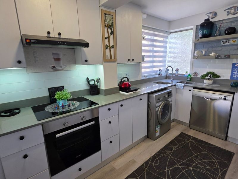 A well-maintained kitchen featuring white cabinetry, modern appliances, a subway tile backsplash, and integrated laundry facilities.