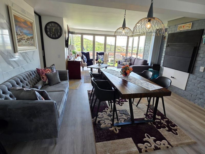 Spacious open-plan living and dining area featuring modern laminate flooring, an exposed brick feature wall, and large sliding doors leading to an outdoor space.