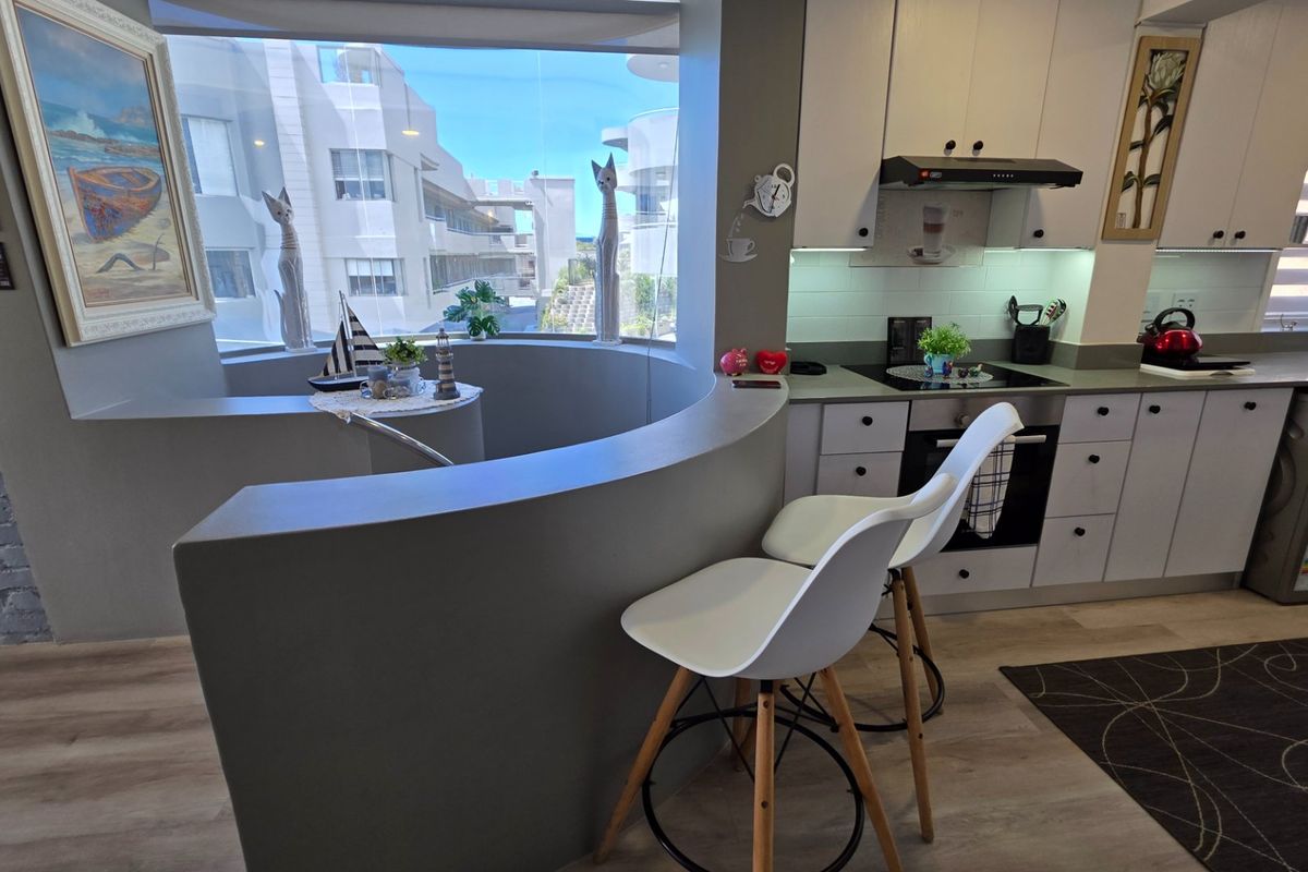 Modern kitchen featuring built-in cabinetry, electric hob, oven, and a unique curved breakfast bar overlooking the exterior view.