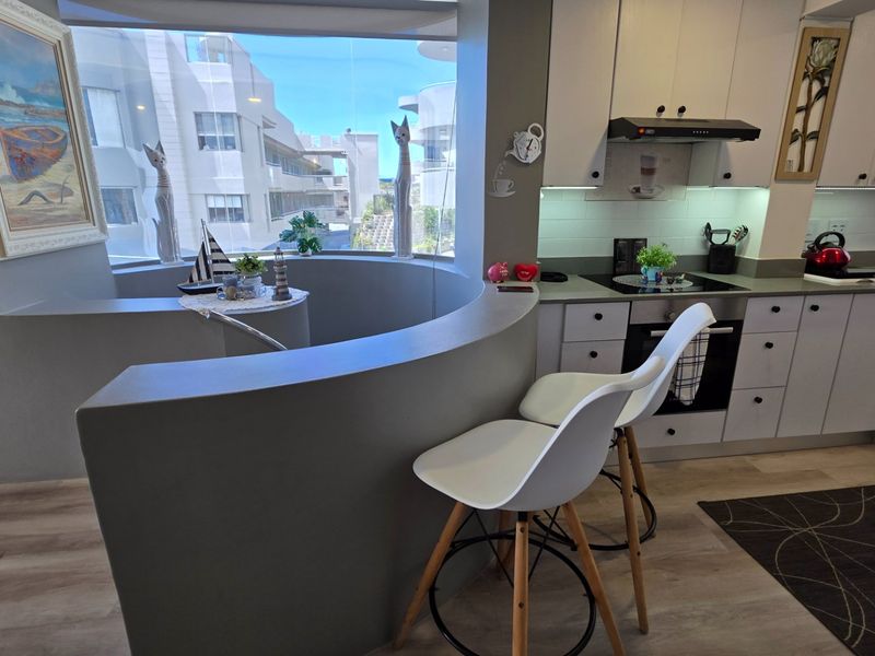 Modern kitchen featuring built-in cabinetry, electric hob, oven, and a unique curved breakfast bar overlooking the exterior view.