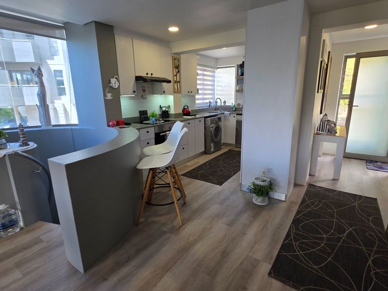 Modern open-plan kitchen featuring sleek built-in cabinetry, integrated appliances, and a breakfast counter, seamlessly flowing into the living area with laminate flooring.