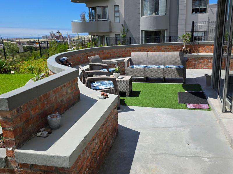 Spacious outdoor patio featuring a curved brick retaining wall with integrated concrete bench seating, artificial turf, and direct access to the apartment interior.