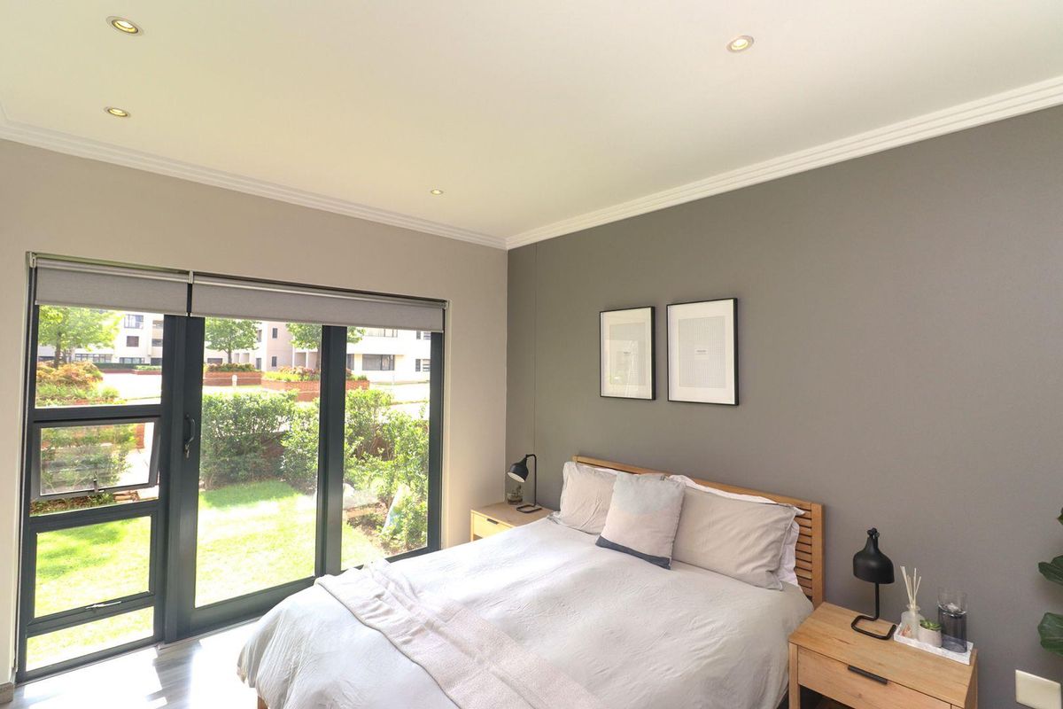 A well-lit bedroom featuring neutral grey walls, crown molding, recessed lighting, and a large sliding glass door providing direct access to the garden area.