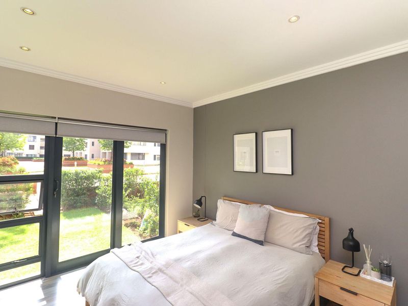 A well-lit bedroom featuring neutral grey walls, crown molding, recessed lighting, and a large sliding glass door providing direct access to the garden area.