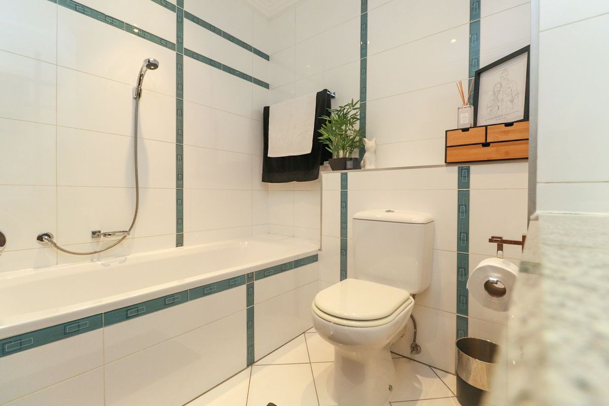 A functional bathroom featuring a bathtub with a handheld shower attachment, a standard toilet, and decorative tiled wall accents.