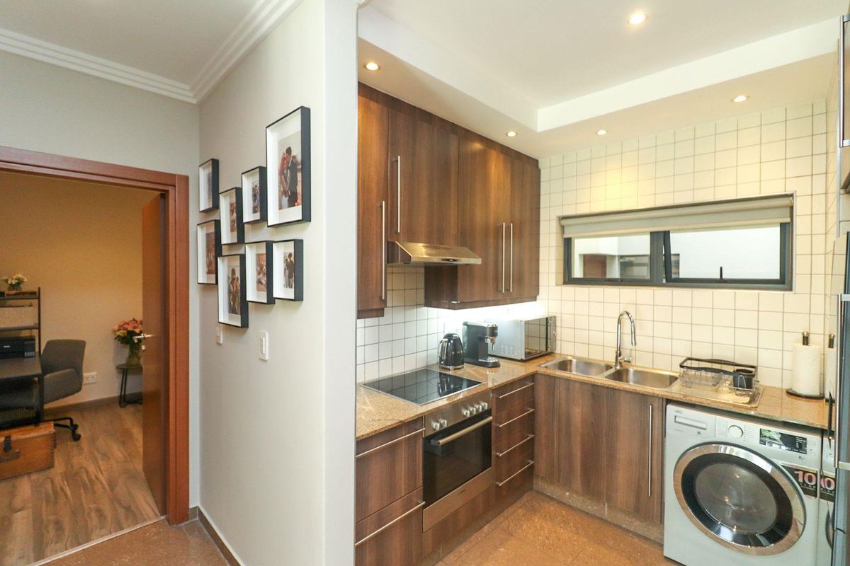 Compact kitchen featuring wood-finish cabinetry, granite countertops, integrated oven and hob, and a tiled backsplash with recessed lighting.
