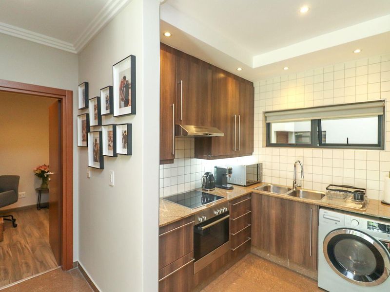 Compact kitchen featuring wood-finish cabinetry, granite countertops, integrated oven and hob, and a tiled backsplash with recessed lighting.