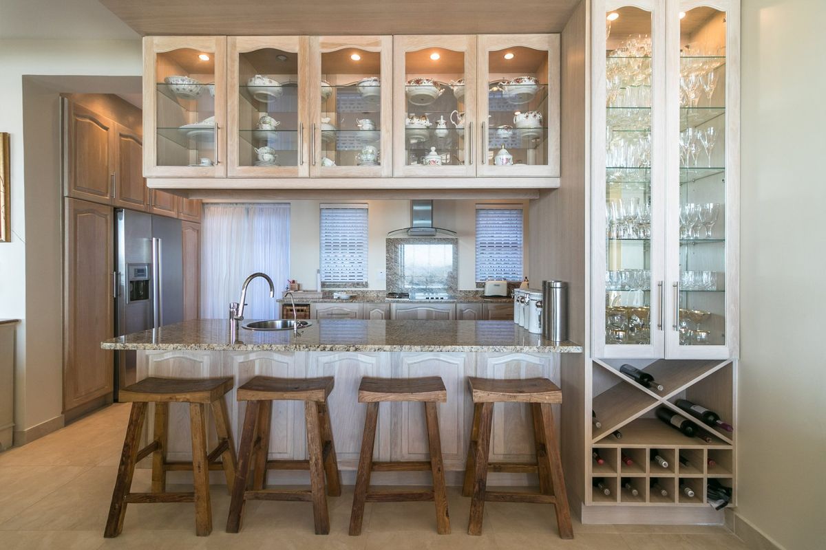 A well-appointed kitchen featuring granite countertops, extensive glass-front cabinetry, integrated wine storage, and a functional breakfast bar with modern lighting.