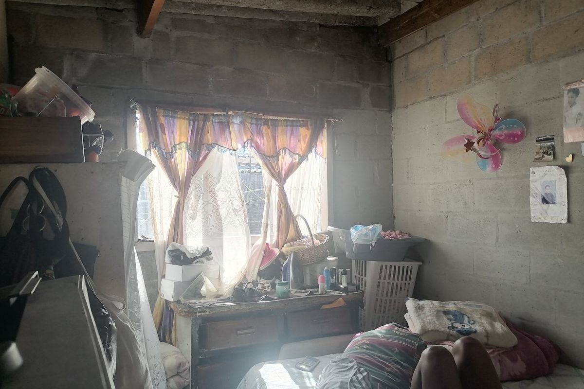 A bedroom featuring exposed concrete block walls and timber ceiling beams, requiring finishing and renovation to improve the overall living space.