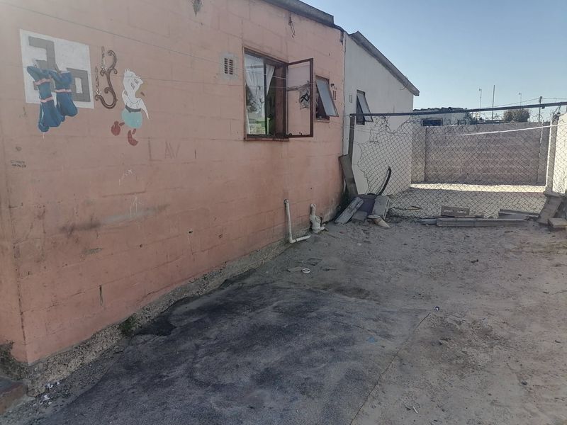 Rear exterior view of the property showing a concrete block wall, chain-link fencing, and exposed external plumbing fixtures.