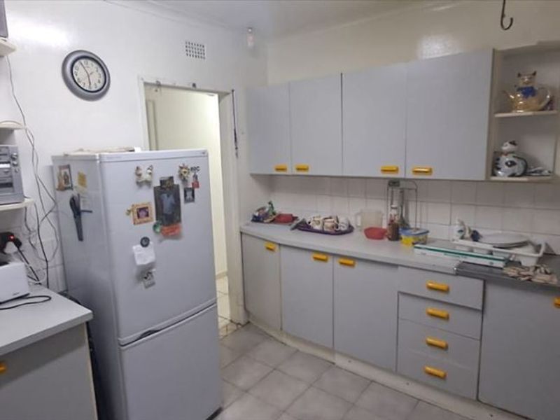 A functional kitchen featuring grey cabinetry, tiled splashbacks, and a stainless steel sink, offering a practical layout with potential for modern updates.