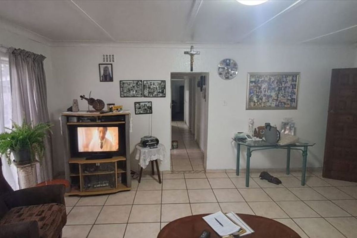 A spacious living room featuring neutral ceramic floor tiles and a central doorway leading to the hallway.