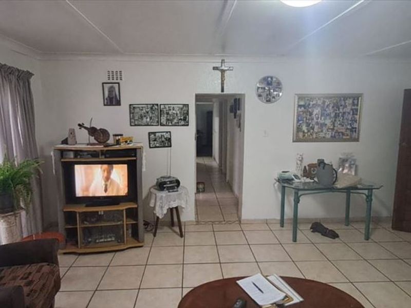 A spacious living room featuring neutral ceramic floor tiles and a central doorway leading to the hallway.