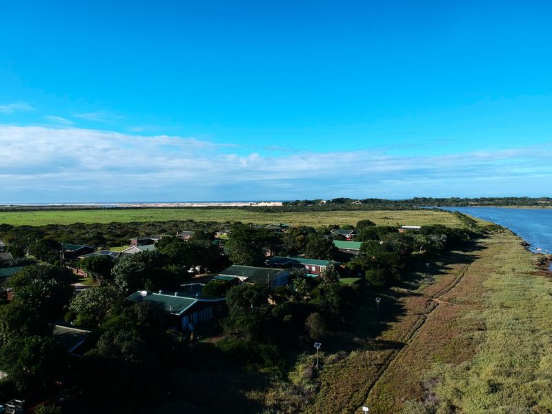 An aerial view of a coastal residential estate situated along a river, showcasing the surrounding natural landscape and proximity to the coast.