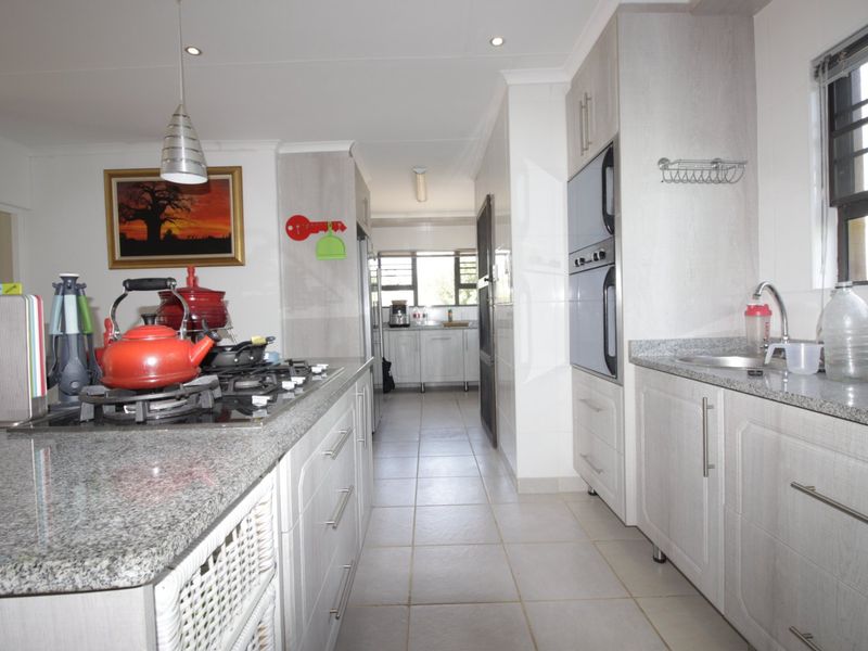A functional kitchen featuring granite countertops, built-in cabinetry, a gas hob, and a double wall oven, with tiled flooring throughout.