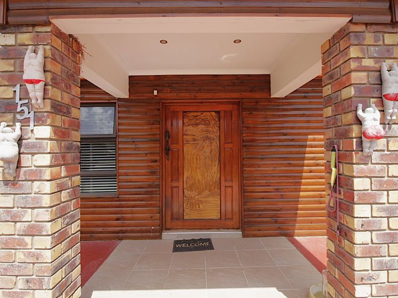 A covered entrance porch featuring brick pillars, timber wall cladding, and a decorative carved wooden front door.