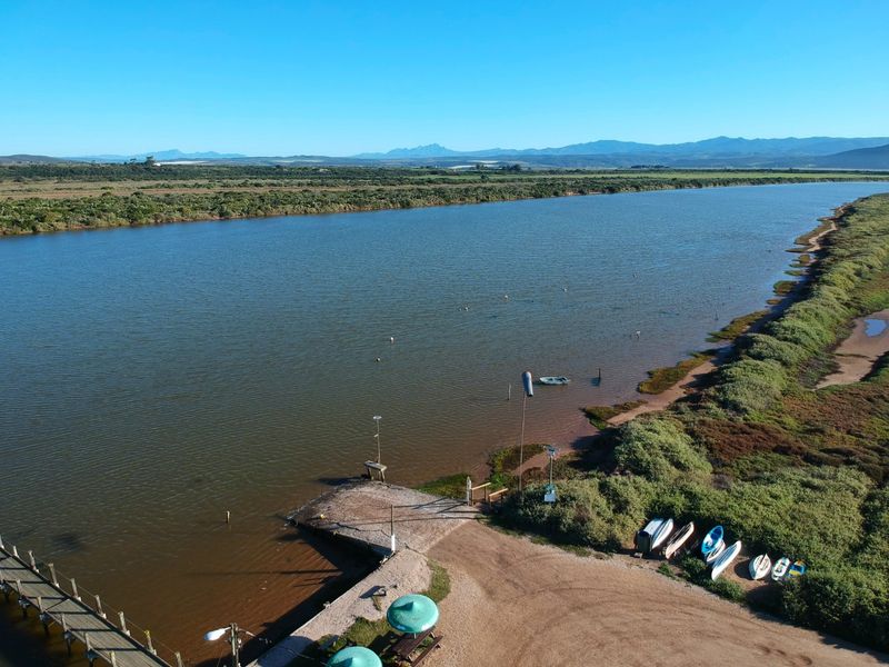 Aerial view of a riverfront property featuring a boat ramp, wooden jetty, and direct access to the water with scenic landscape views.