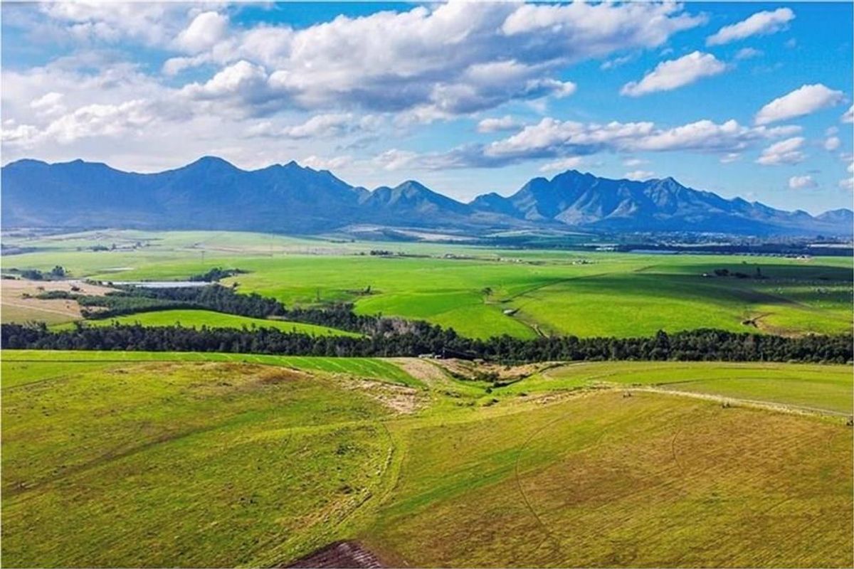 An expansive aerial view of lush green farmland and rolling pastures set against a dramatic mountain range backdrop.