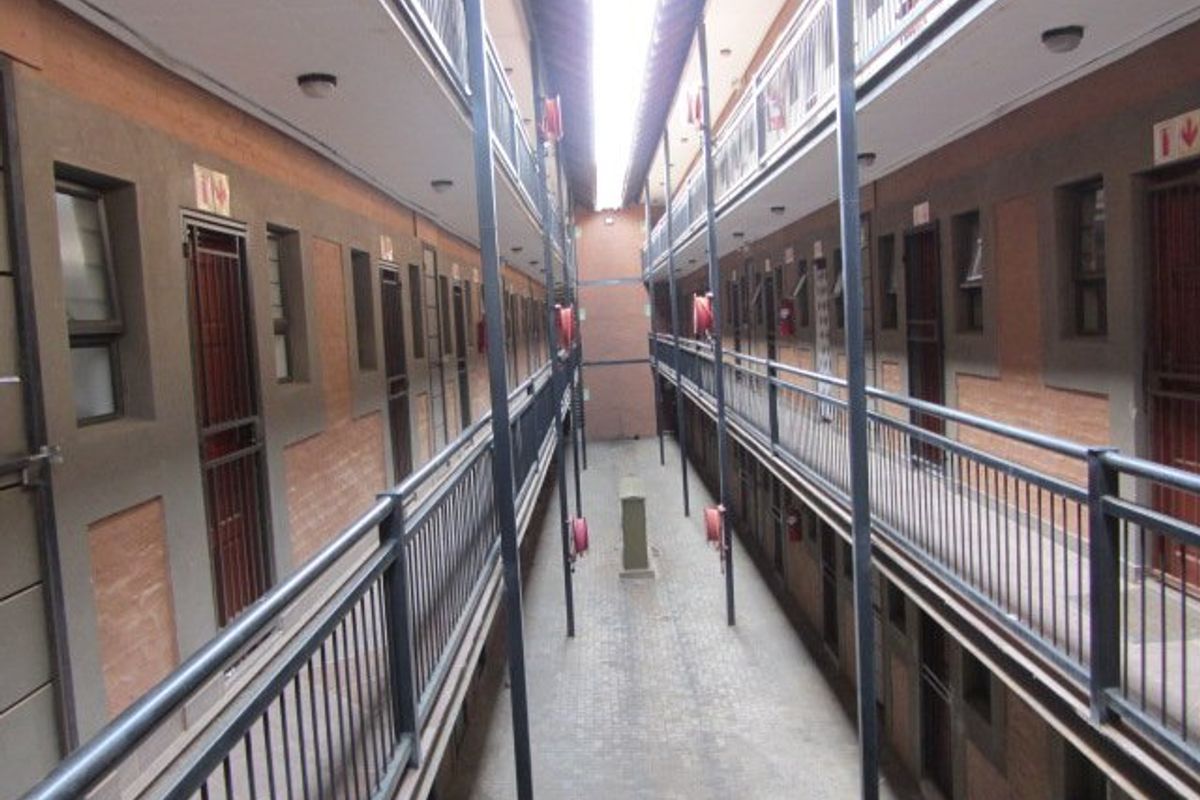 An exterior view of an apartment complex courtyard featuring multi-level walkways, metal security railings, and brick facade construction.