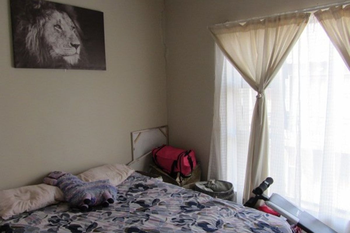 A bedroom featuring neutral wall paint and a window with curtains, showing minor signs of wear including a visible crack in the wall plaster.
