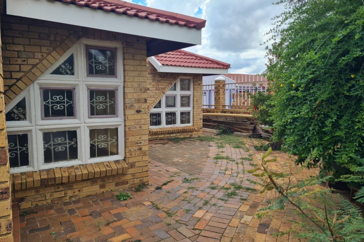 Rear exterior view of the house featuring face brick walls, tiled roofing, and a paved patio area with security-fitted windows.