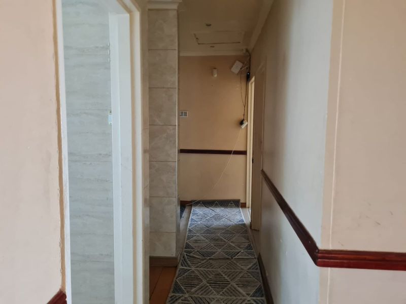 A narrow residential hallway featuring chair rail molding, tiled wall accents, and recessed lighting, currently showing signs of wear and exposed wiring.