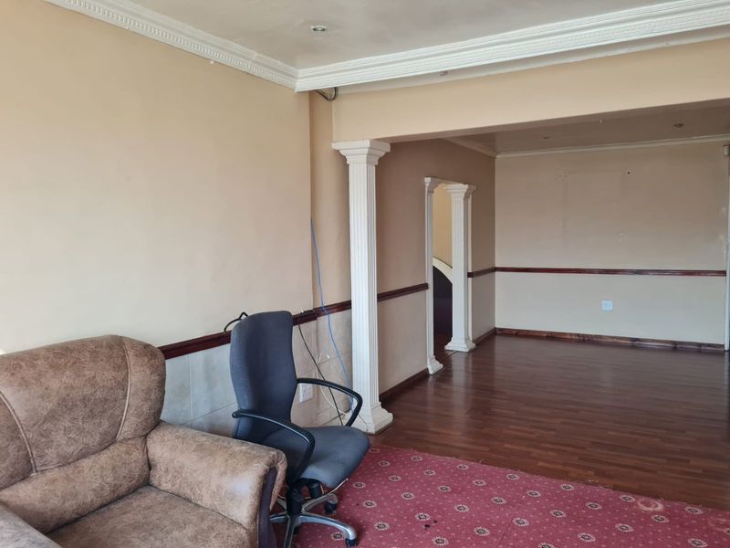 Spacious living area featuring decorative columns, crown molding, and laminate flooring, offering a versatile layout with potential for modern updates.